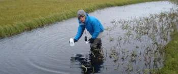 a person standing in a body of water holding a bottle