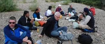 a group of people sitting on top of a rocky field near a river