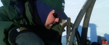 a man in a green jacket working on a machine in the snow