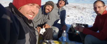 a group of people sitting on top of snow covered ground, eating